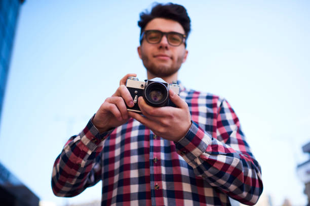 istock Selective focus on vintage camera in hands of hipster guy standing outdoors, young handsome traveler fond of photography taking pictures on old retro equipment during free time on city street 1157859678