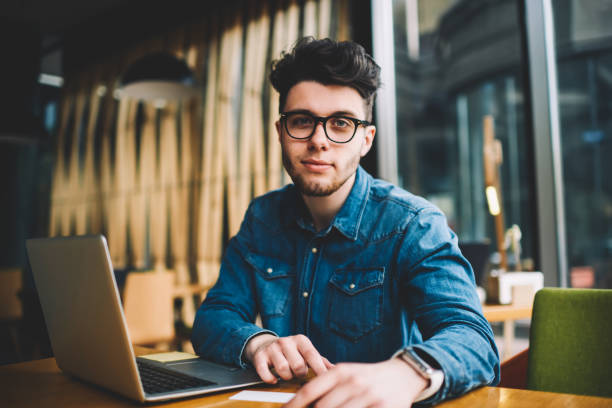 istock Portrait of skilled male it developer working remotely in cafe interior using wireless connection and laptop computer,young man in spectacles for vision protection while learning via netbook 1157859764