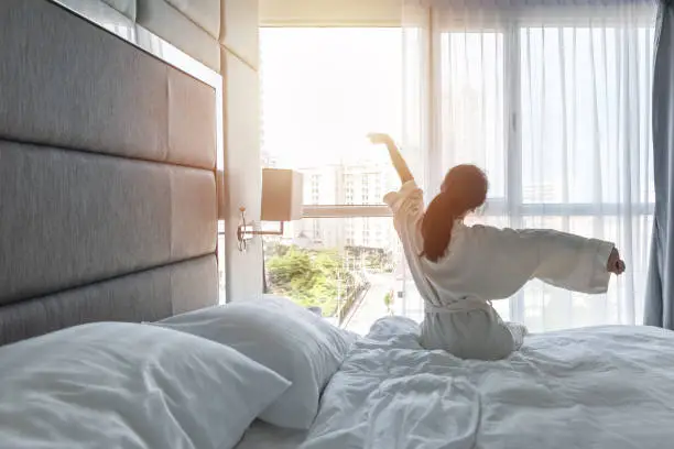 Hotel room comfort with good sleep easy relaxation lifestyle of Asian girl on bed have a nice day morning waking up, taking some rest, lazily relaxing in guest bedroom in city hotel