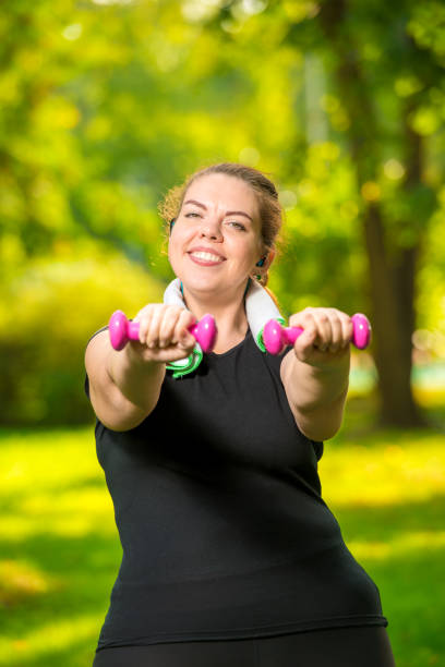 istock overweight woman doing her exercise in the park, exercise with dumbbells 1157867281
