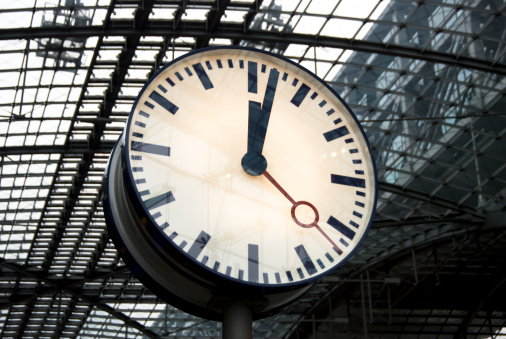 Modern clock face in front of a futuristic steel construction in a train station