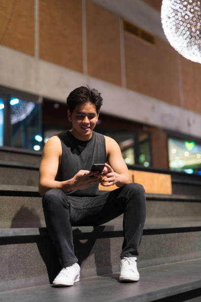 istock Young happy Asian man using phone in the city outdoors at night 1157881476