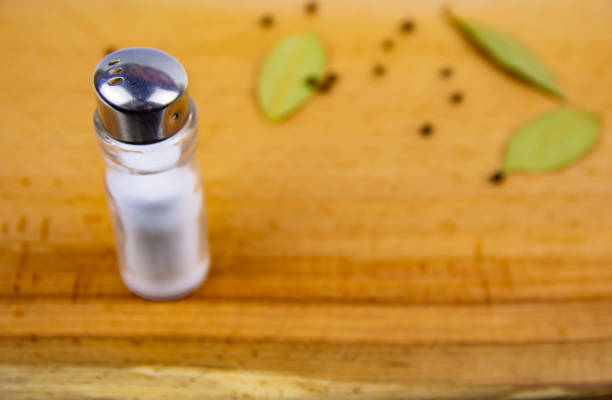 salt and pepper in spoon and shakers, bay leaves on rustic wooden table