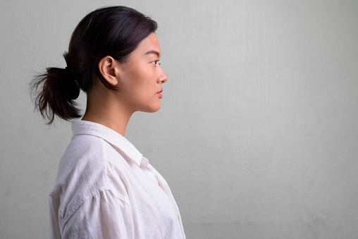 Studio shot of young beautiful Asian woman with hair tied against white background