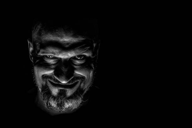 Face with a bearded man grimace against a dark background with sharp shadows. Comedic, fabulous villain or negative character conception with copy space.