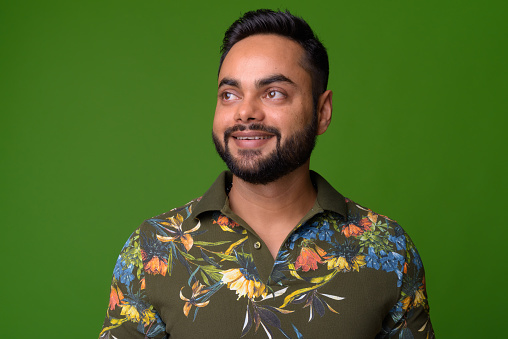 Studio shot of young bearded Indian man against chroma key with green background