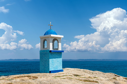 Traditional Greek small church or chapel. Blue sky with white clouds and sea in background