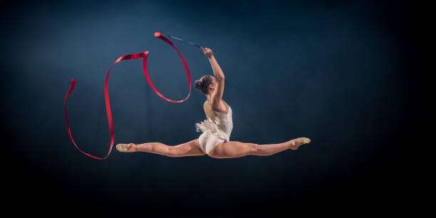 gymnast doing rhythmic gymnastics with red ribbon - the splits ethnic women exercising imagens e fotografias de stock