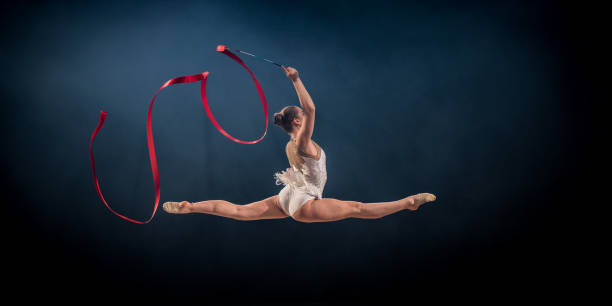 гимнастка делает художественной гимнастики с красной лентой - skill side view jumping mid air стоковые фото и изображения