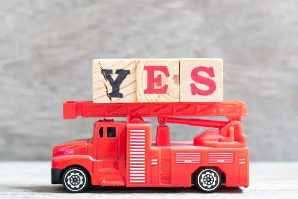 Photo of Red fire truck hold letter block in word yes on wood background
