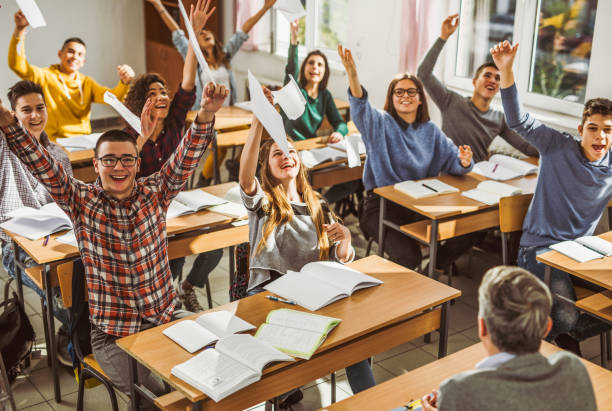 istock Happy students throwing papers while celebrating the end of a school year in the classroom. 1157906329