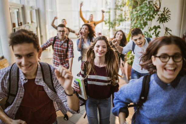 Large group of cheerful students running through school hallway. Large group of high school students running to class through a hallway. Focus is on happy student looking at camera. boy and girl looking at camera stock pictures, royalty-free photos & images