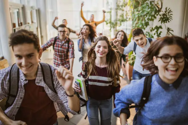 Large group of high school students running to class through a hallway. Focus is on happy student looking at camera.