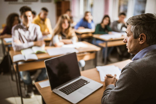 istock Profile view of serious professor teaching a lecture at high school. 1157907647