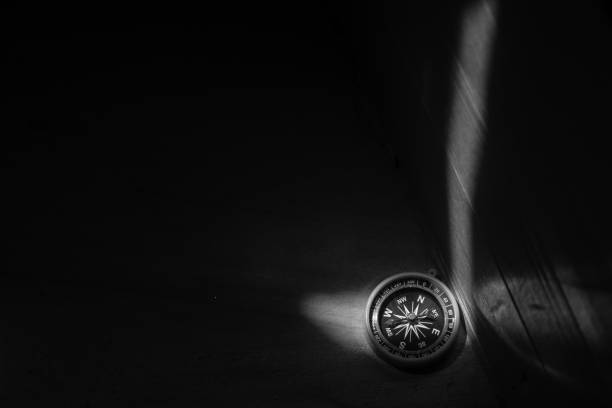 Black and White Image of Compass on the dark wood surface with a light spot.