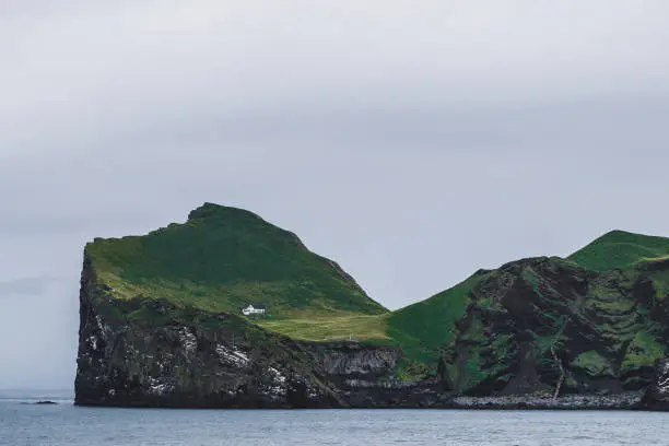 Photo of Lonely house on Ellidaey island in Vestmannaeyjar archipelago, Iceland. Rocky and green island. Nordic landscape.