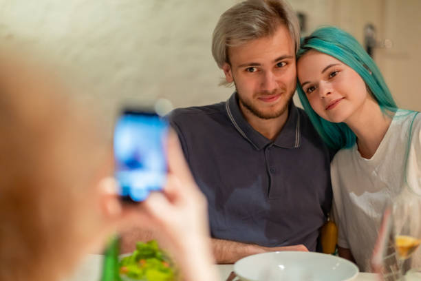 Anime-like couple posing for the photo taken by flatmate Anime-like young couple posing for the photo taken at dinner table by their flatmate on mobile phone flatmate stock pictures, royalty-free photos & images
