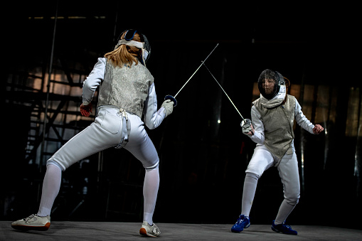Fencer female athletes fighting against black background during a Sporting Event.