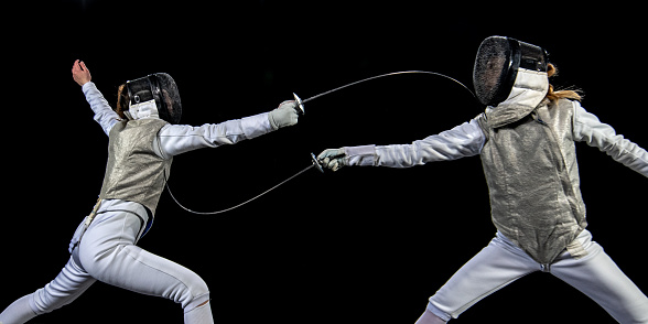 Female fencer athletes fighting against black background during a Sporting Event.