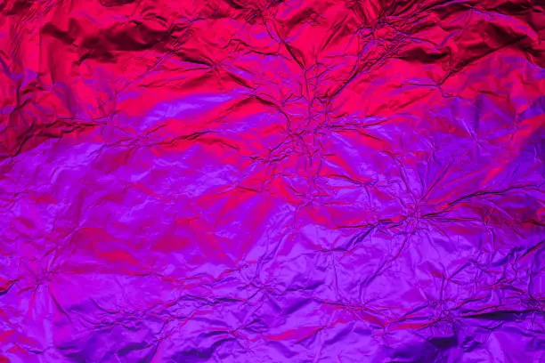 Purple red deformed background made of neon lights foil. Trendy duotone texture.