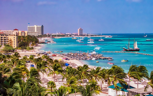 View of beautiful Palm beach in the tropical island of Aruba, with yachts and tour boats anchored in the turquoise coastal waters of the Caribbean sea.