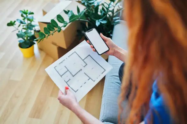 Close up of new apartment plans and smartphone being held by young woman