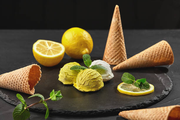 Tasty creamy and lemon ice cream decorated with mint served on a stone slate over a black background.