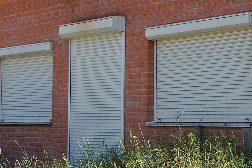 the door and windows are closed by white rolls on a brown brick wall in green grass