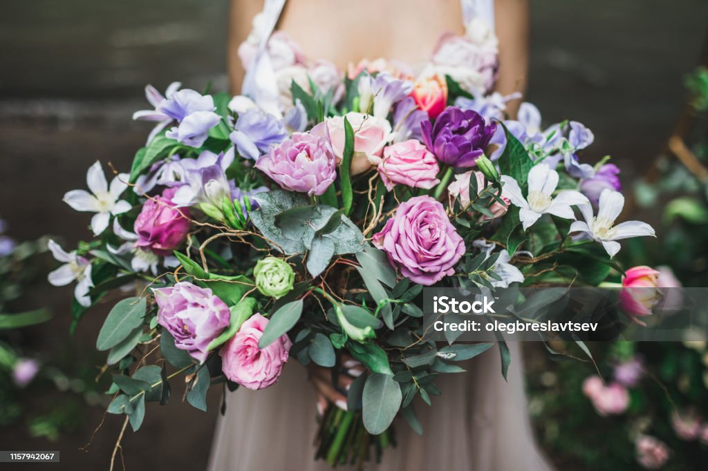 Bride holding b beautiful colorful wedding bouquet of roses, peonies and tulips in bright pink, coral and purple colors. Wedding Stock Photo