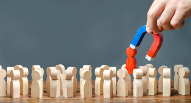 istock A hand with a magnet pulls a red human figure out of the crowd. Identify disloyal, repression, dissent. toxic, non-competent worker. leader manages the business. Search for enemies and spies. 1157942840