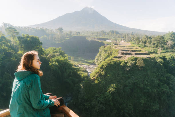 istock Woman looking at Kedung Kayang waterfall and Merapi mountain on Java 1157944610