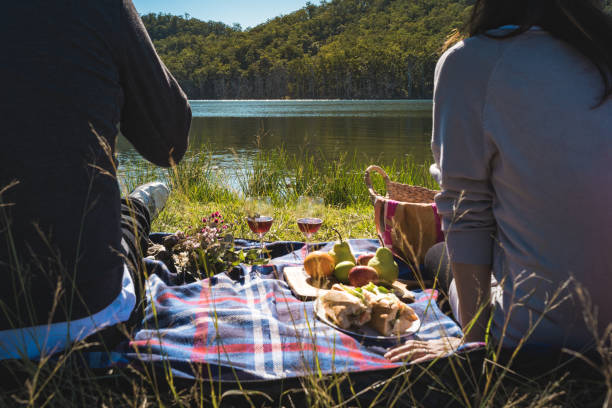 back style couple having picnic on sunny day weekend in Autumn with baguette sandwich fruits wine picnic basket bring my bottle stock photo