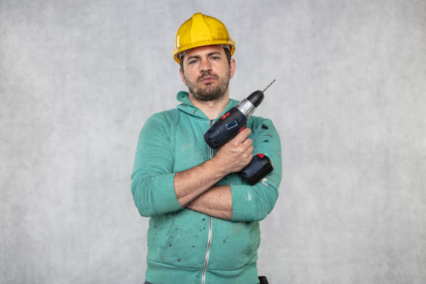 Low angle shot of a construction worker using a screw gun to drill holes in a wood stud wall on a white background.