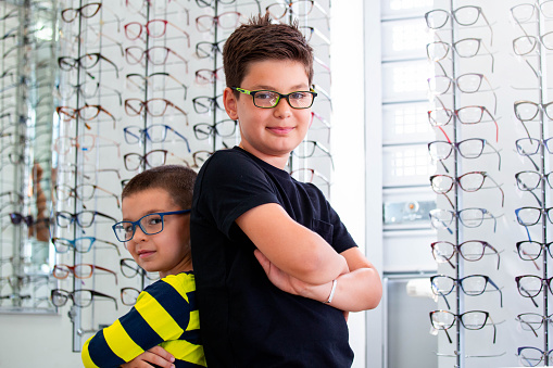 Health care, eyesight and vision concept - two boys choosing glasses at optics store.