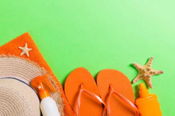 istock Summer beach flat lay accessories. Sunscreen bottle cream, straw hat, flip flops, towel and seashells on colored Background. Travel holiday concept with copy space 1157948692