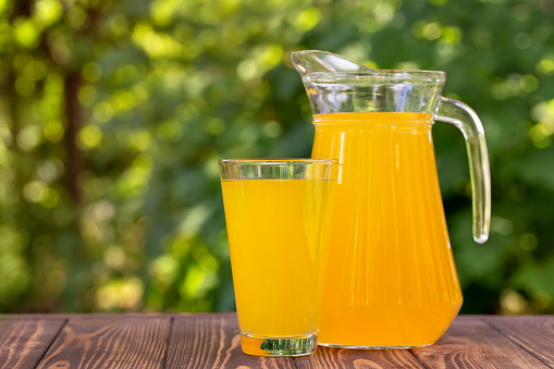orange juice in glass and jug on wooden table outdoors. Summer refreshing drink
