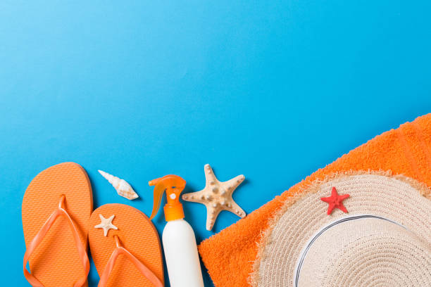 istock Summer beach flat lay accessories. Sunscreen bottle cream, straw hat, flip flops, towel and seashells on colored Background. Travel holiday concept with copy space 1157948757