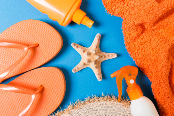 istock Summer beach flat lay accessories. Sunscreen bottle cream, straw hat, flip flops, towel and seashells on colored Background. Travel holiday concept with copy space 1157948955