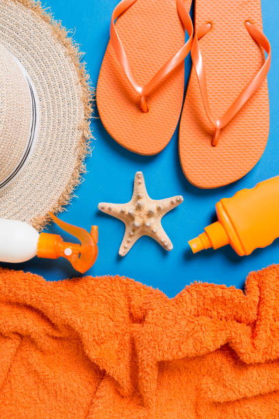 istock Summer beach flat lay accessories. Sunscreen bottle cream, straw hat, flip flops, towel and seashells on colored Background. Travel holiday concept with copy space 1157949116