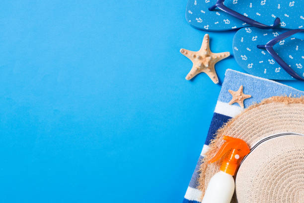 istock Summer beach flat lay accessories. Sunscreen bottle cream, straw hat, flip flops, towel and seashells on colored Background. Travel holiday concept with copy space 1157949327
