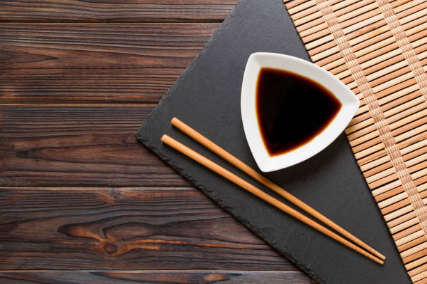 chopsticks e molho de soja na placa de pedra preta, fundo de madeira com espaço da cópia - black dishware sushi isolated - fotografias e filmes do acervo