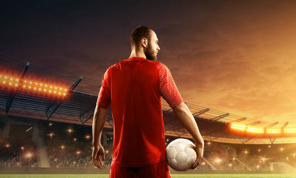 istock Soccer player with a ball on a floodlit stadium. Back view 1157949661