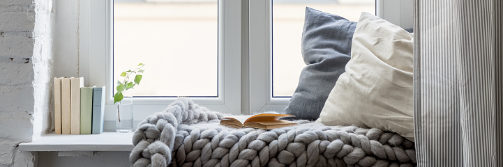Relaxation area with books, pillows and cozy blanket on a wooden windowsill, panorama