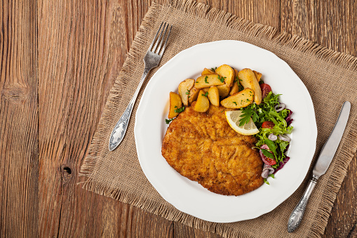 Chicken schnitzel, served with roasted potatoes and salad. Top view. Natural wooden background