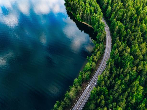 Aerial view of road between green forest and blue lake in Finland stock photo