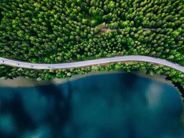 Photo of Aerial view of road between green forest and blue lake in Finland