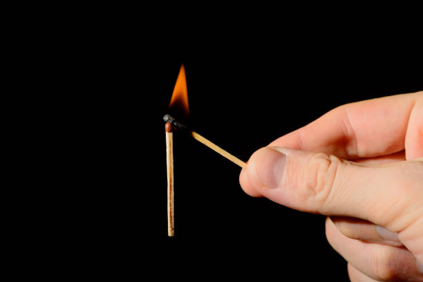 istock A hand with a lit match sets fire to a new match on a black background. 1157956618