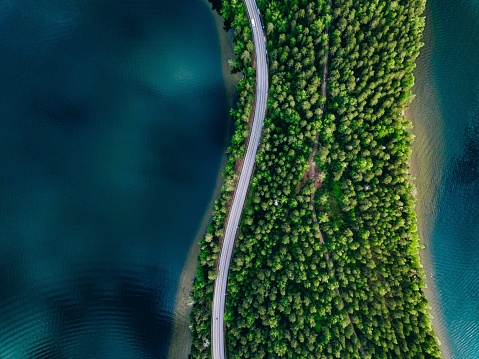 Aerial view of road between green forest and blue lake in Finland