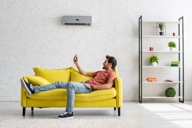 istock handsome young man lying on yellow sofa under air conditioner and holding remote control 1157958015