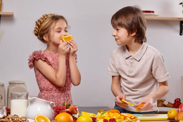 Cute kids are cooking together in a kitchen against a white wall with shelves on it. stock photo